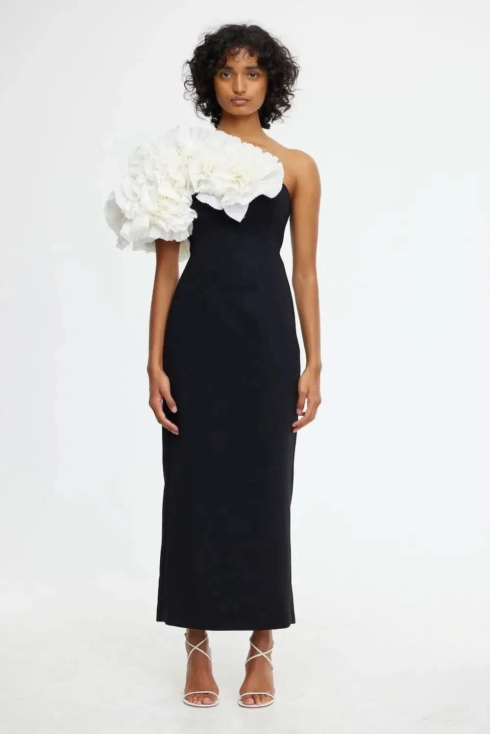 A woman wearing a black Hampstead Midi Dress with a one-shoulder design and a floral headpiece.