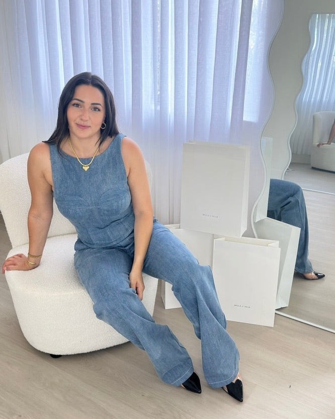 Woman wearing a matching blue denim co-ord set with sleeveless top and wide-leg jeans, seated in a bright room, styled by BELLA n' BEAR.