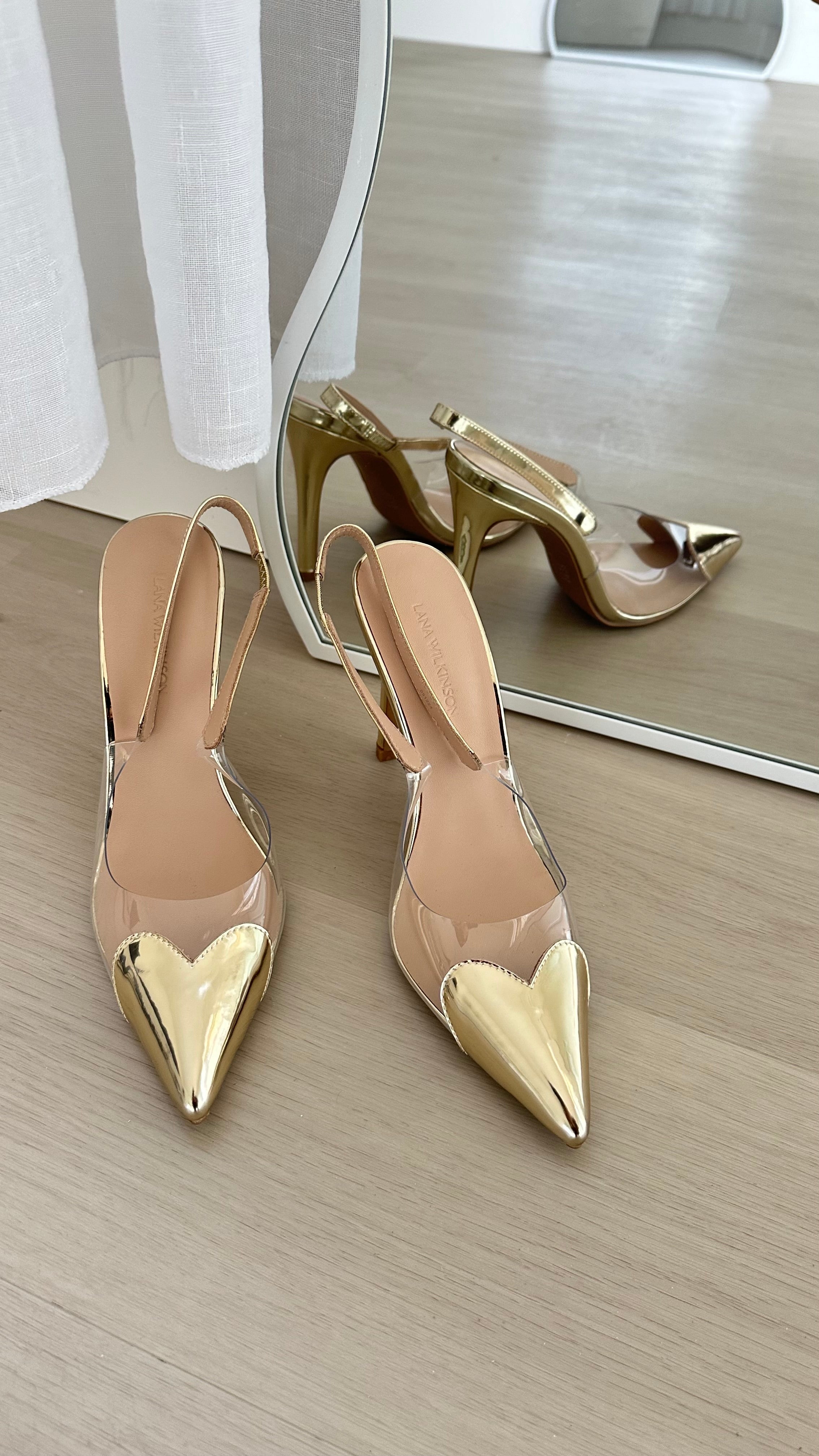 a pair of gold Lana Wilkinson Rhiannon shoes sitting on top of a wooden floor