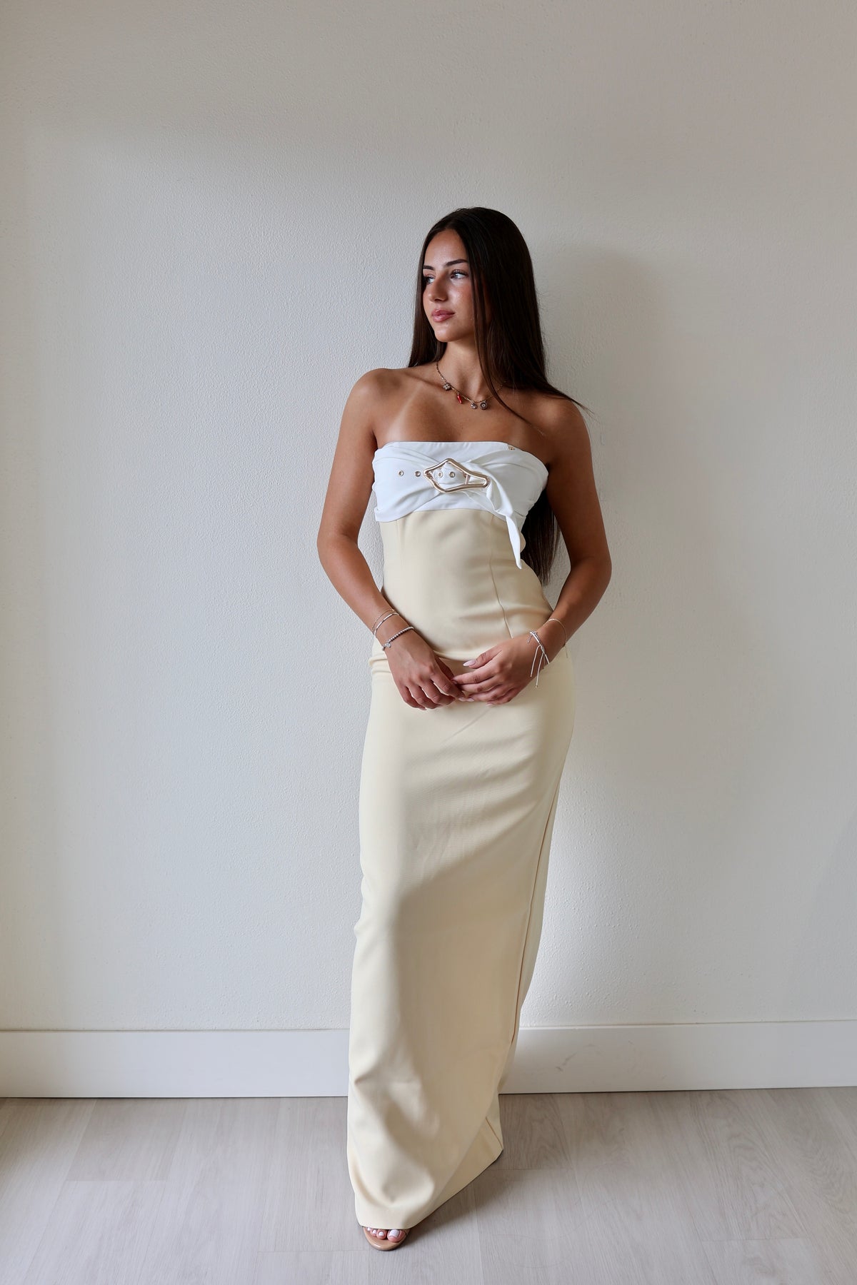 Kasai dress in cream with a strapless design and decorative belt detail, worn by a model against a plain background.