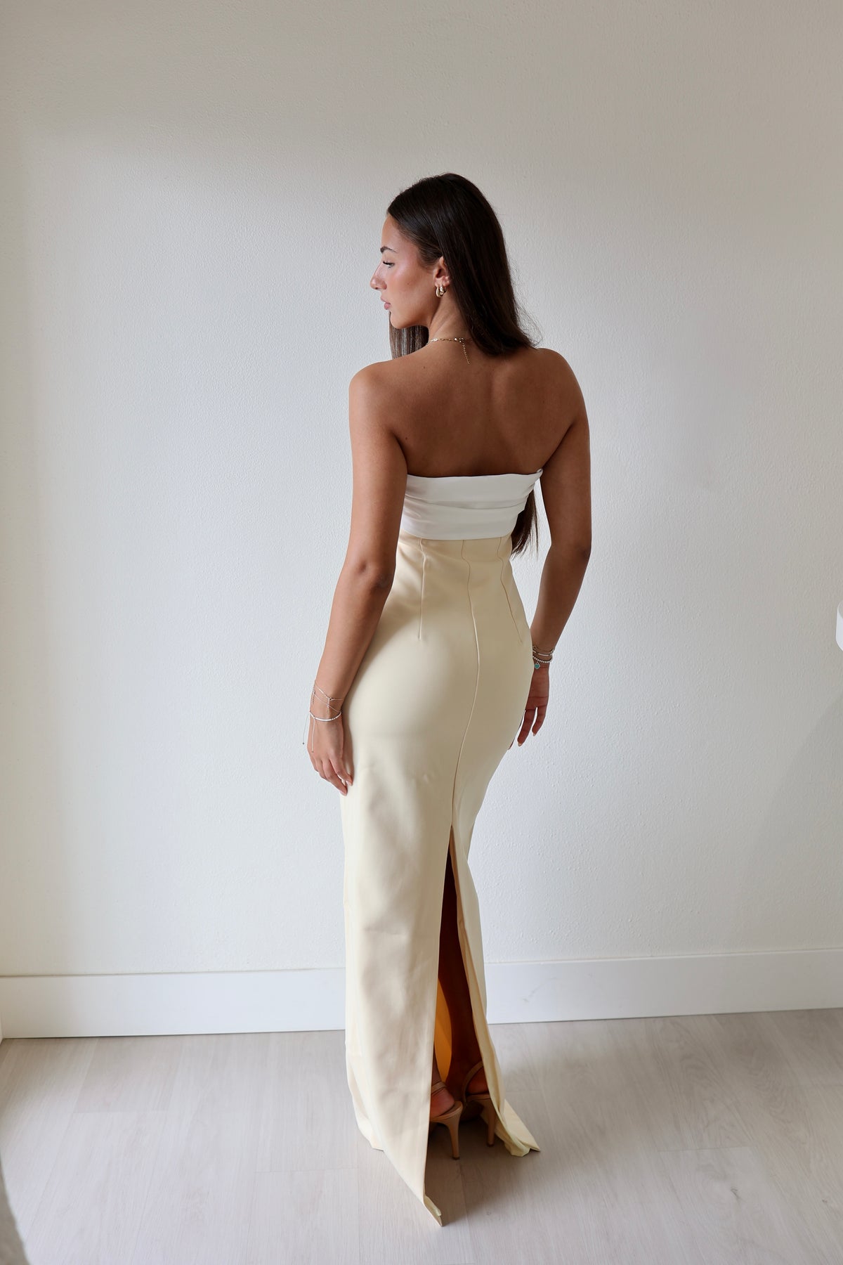 Kasai dress in cream with a fitted bodice and side slit, shown from the back against a plain wall.