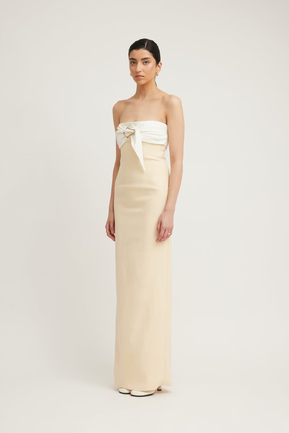 Strapless cream maxi dress with a white bow detail at the waist, worn by a model against a neutral background.