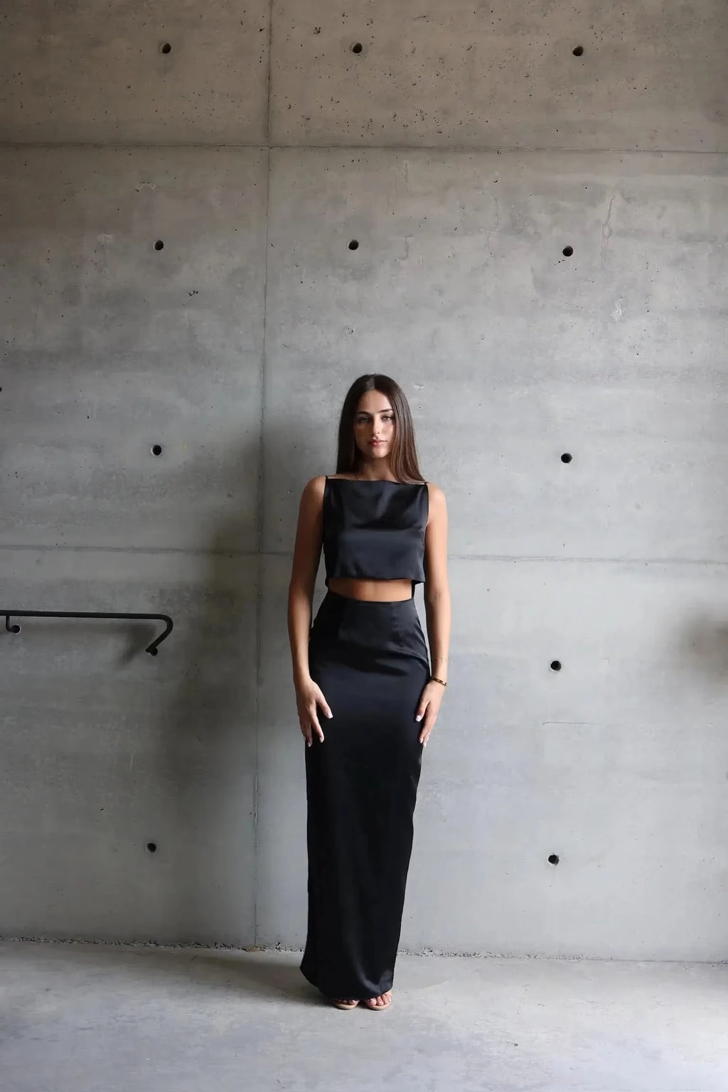 Woman in a black outfit standing against a concrete wall.