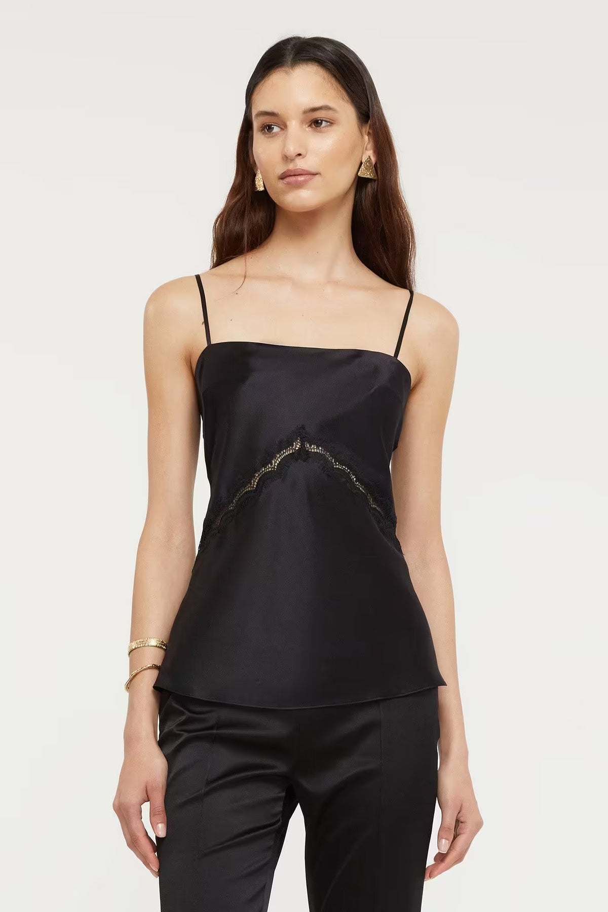 Black Nomie Cami top with thin straps, featuring a subtle lace detail along the front, worn with black pants.