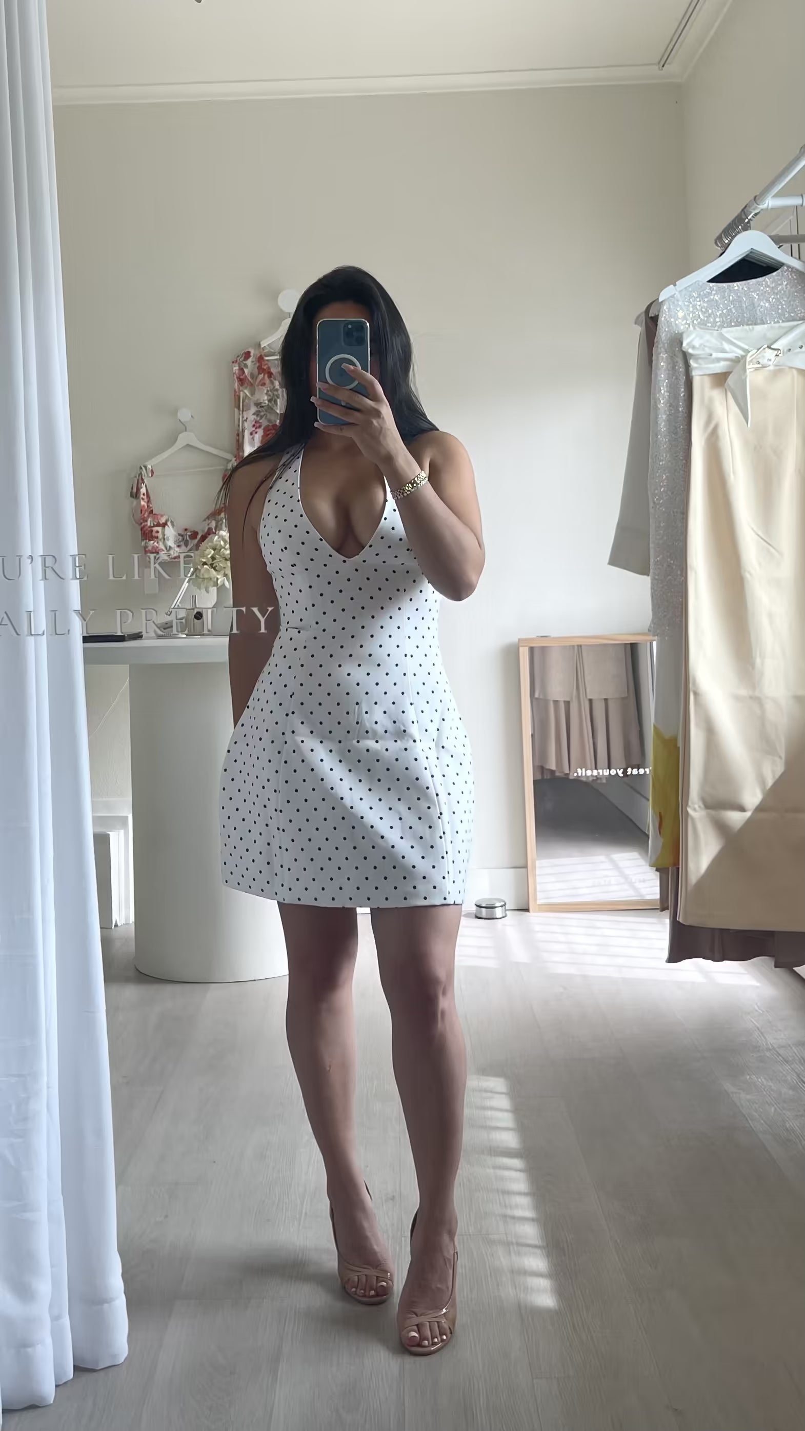 Woman taking a mirror selfie wearing a polka dot dress in a room.