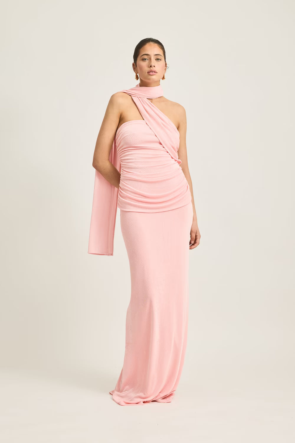 Iesha dress in soft pink, featuring a one-shoulder design and draped fabric, worn by a model against a neutral background.