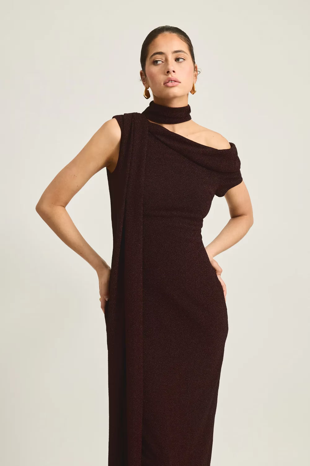 Izara dress in dark burgundy with a one-shoulder design and draped fabric, styled on a model against a neutral background.