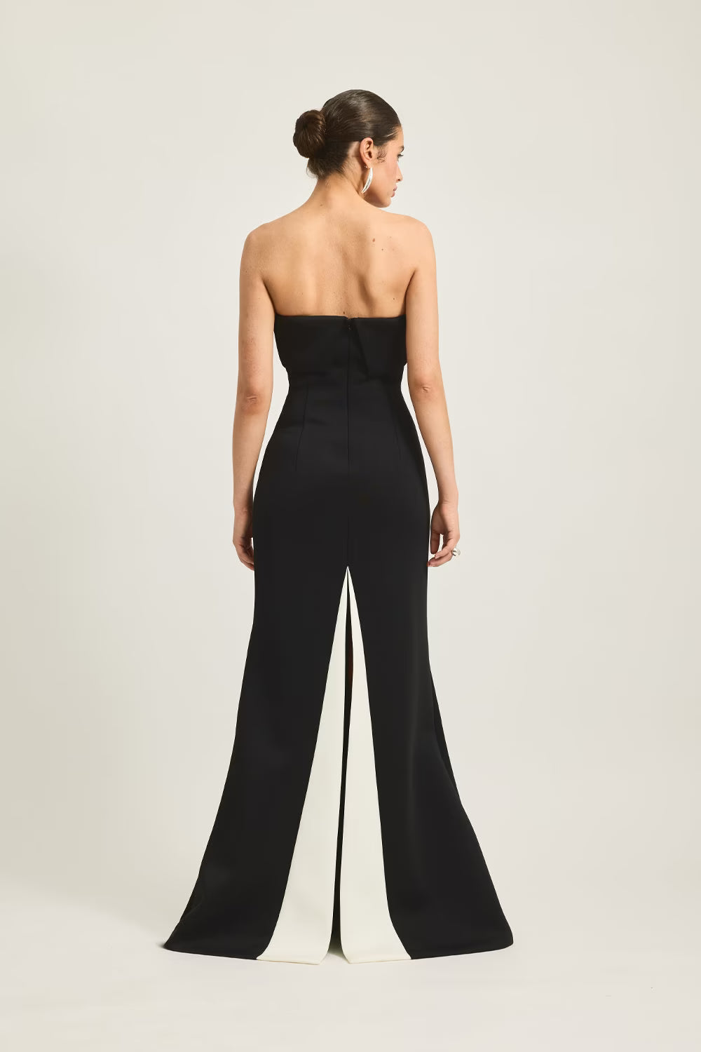 Stellan gown in black with a white split at the back, featuring a strapless design and a fitted silhouette.