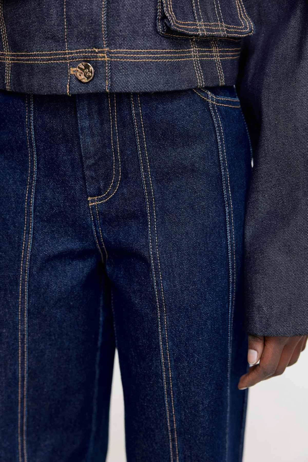 Dark indigo denim jeans close-up, stitched panel lines, metal button front