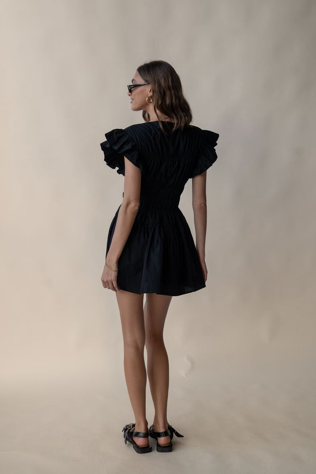Black mini dress with flutter sleeves and gathered skirt, shown from side