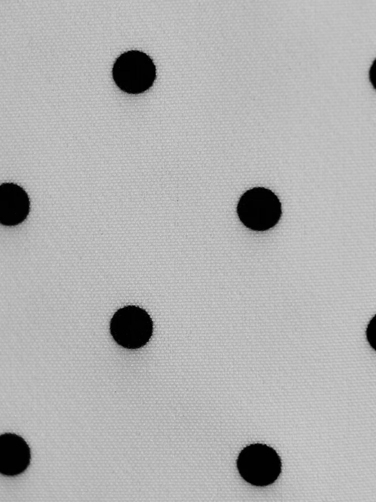 White fabric with scattered black polka dots, close-up pattern detail