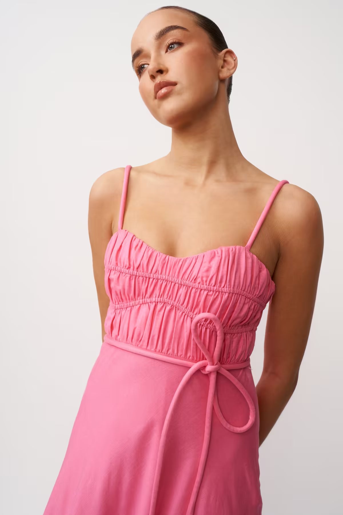 Close-up of pink sleeveless dress: gathered square neckline and tie waist with drawstring bow.