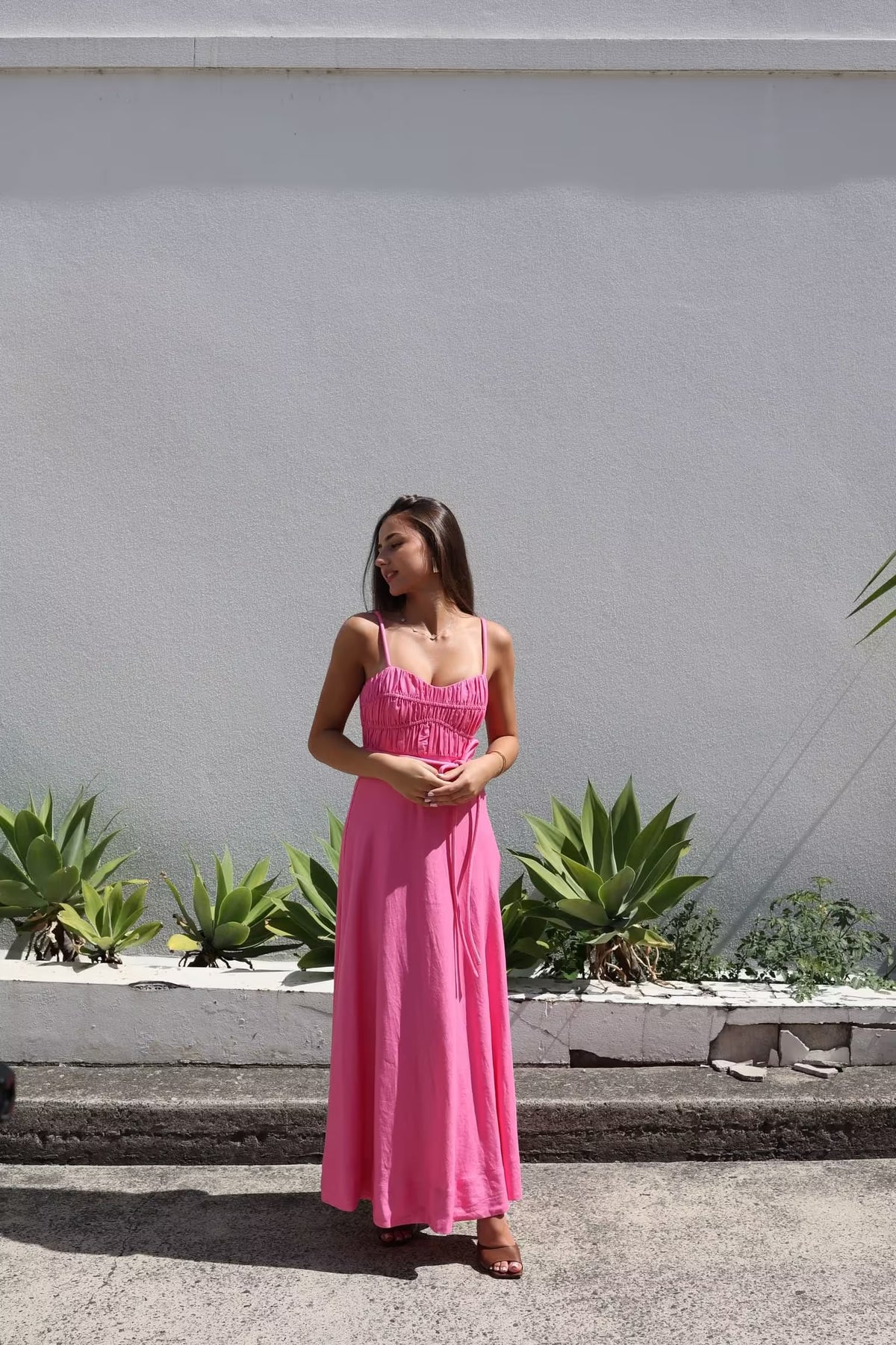 Pink midi panel dress with spaghetti straps, gathered bust, and tied waist in a flowing skirt.