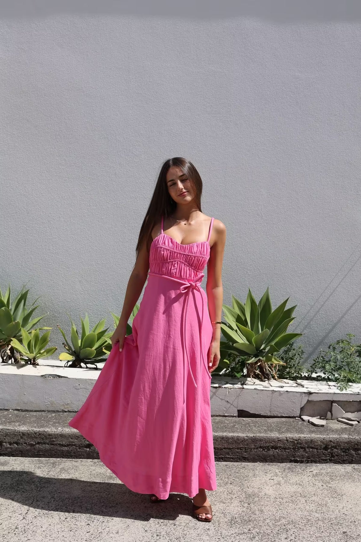 Pink midi panel dress with thin straps, smocked bust, and tied waist with loose skirt.