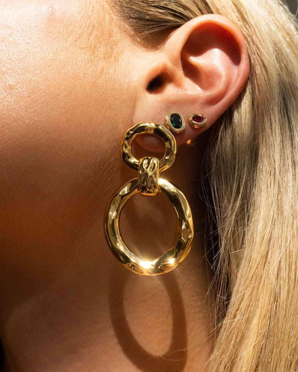 Gold hammered loop hoop earrings on ear with gemstone accents in red, green, and blue