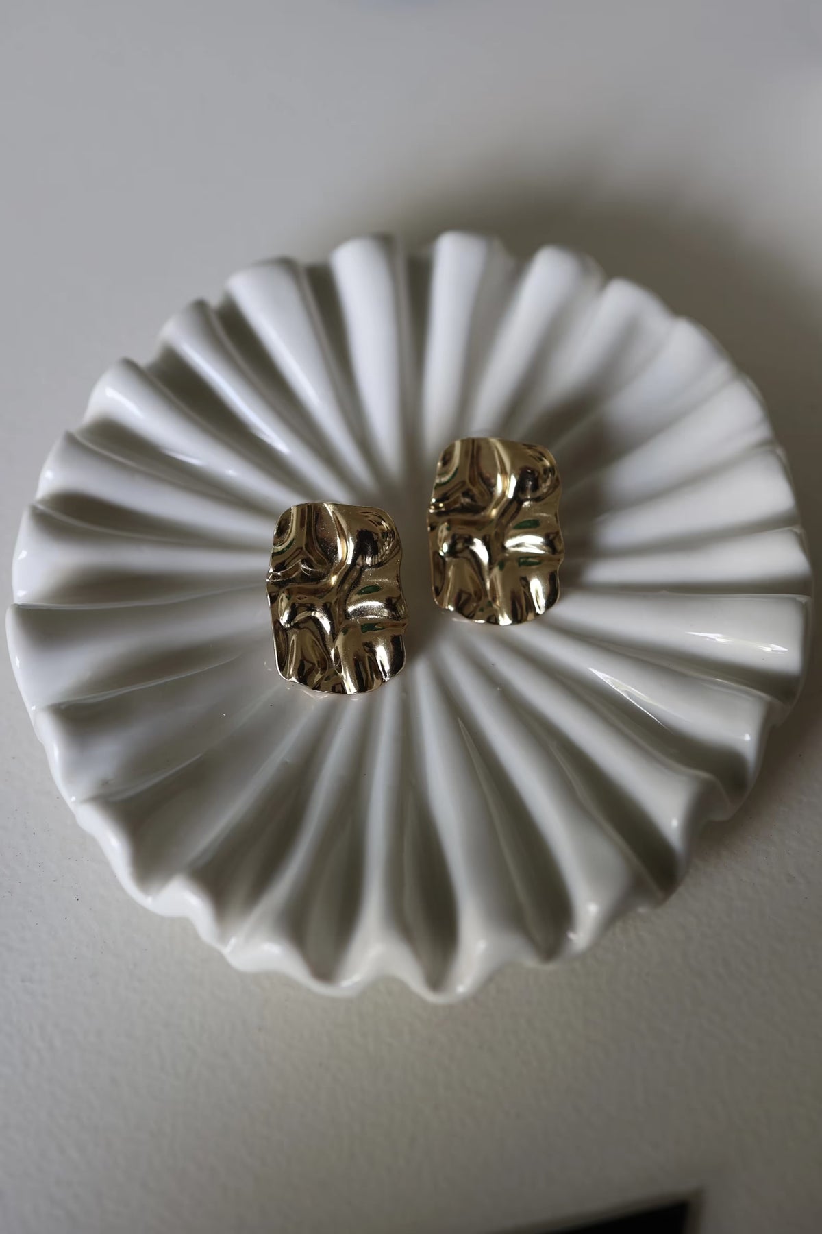 Gold textured square stud earrings on a white scalloped backing