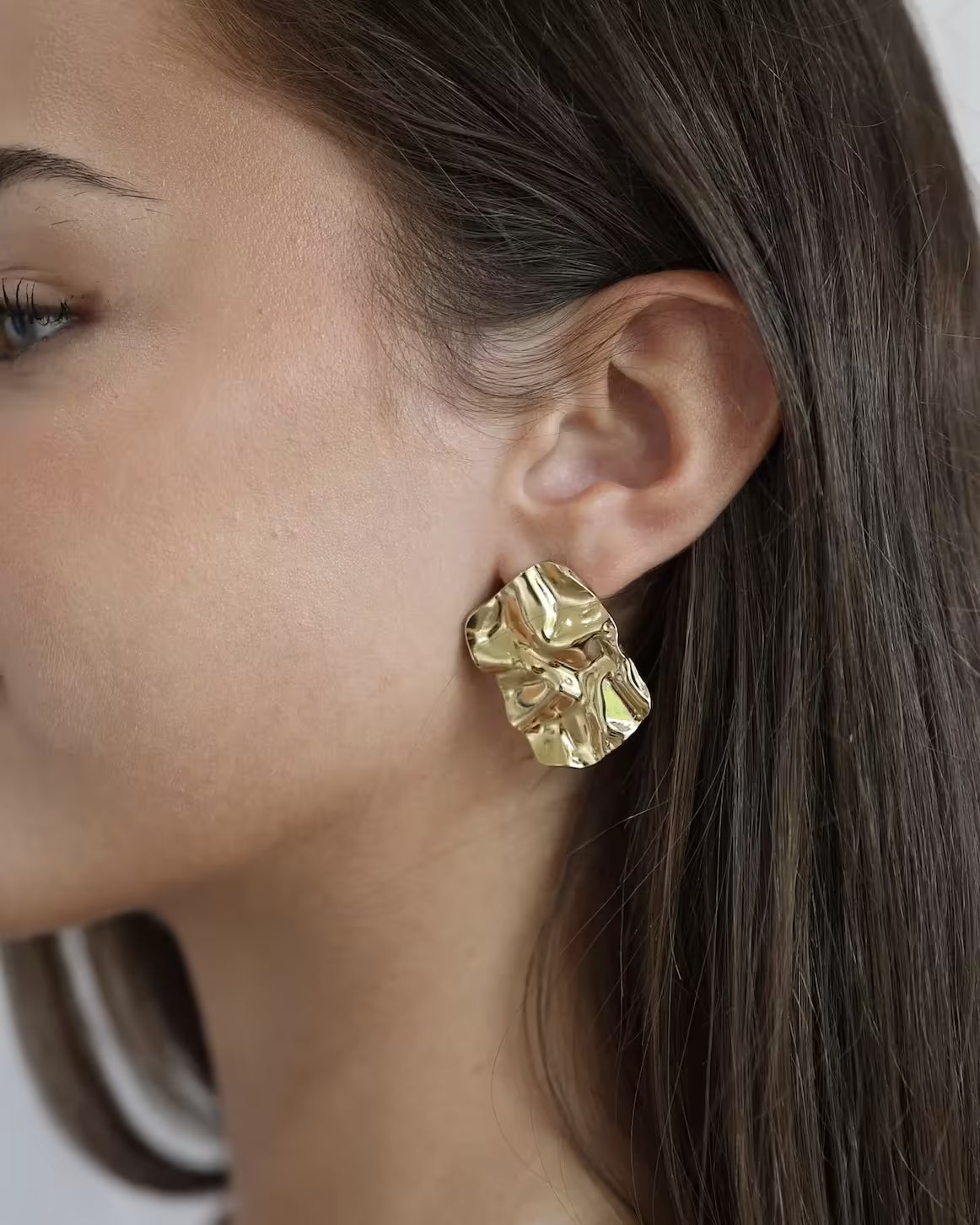 Gold sculpted square stud earrings on ear