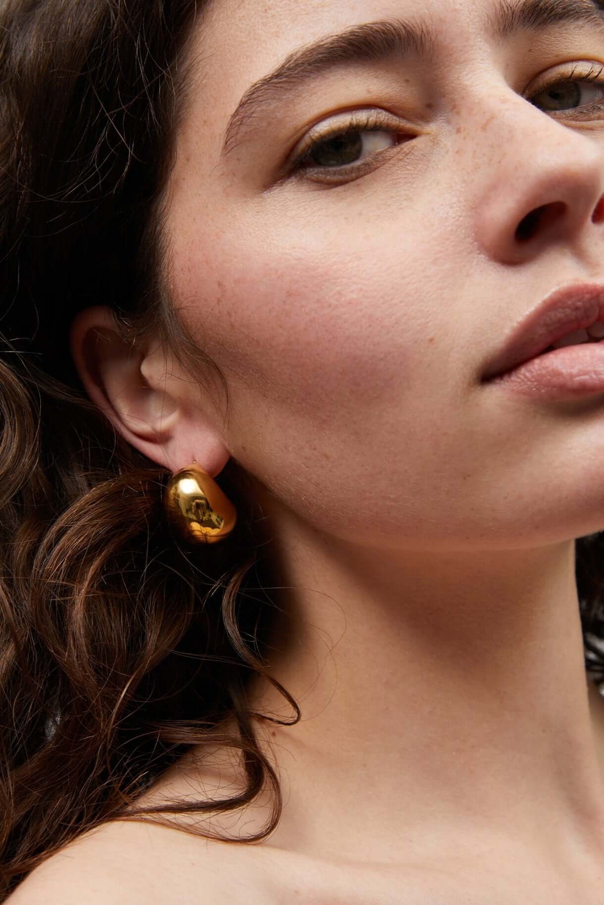 Gold dome stud earrings on ear with visible post