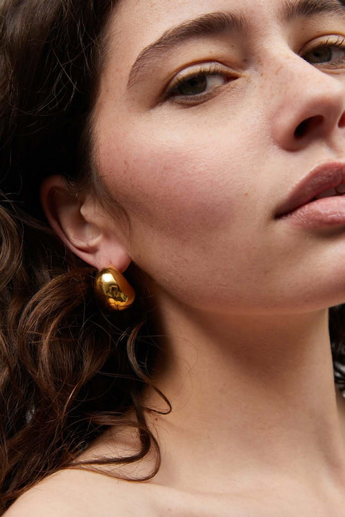 Gold dome stud earrings on ear with visible post
