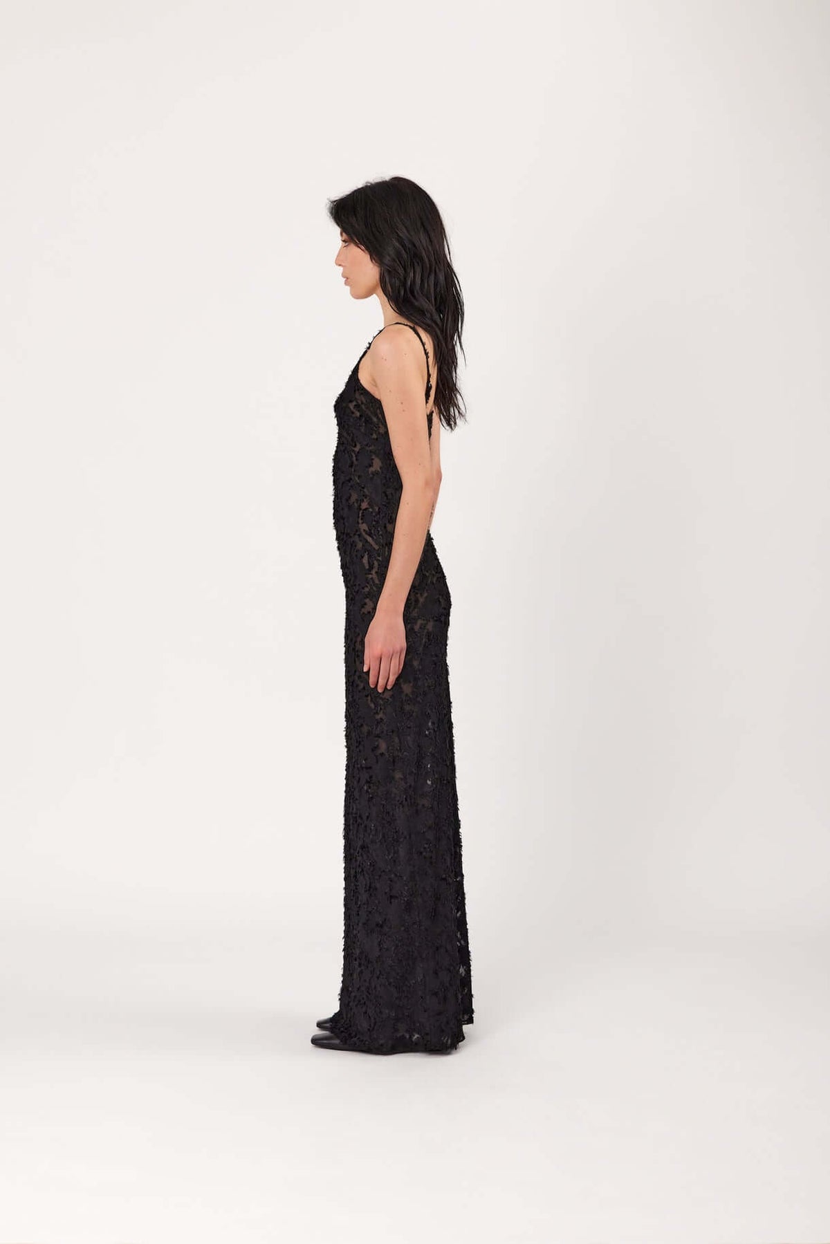 Black lace slip dress viewed from side, spaghetti straps, long fitted maxi length