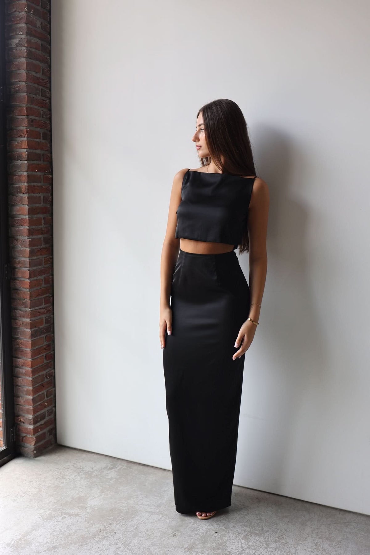 Black sleeveless crop-top gown with long column skirt, back-leaning side view