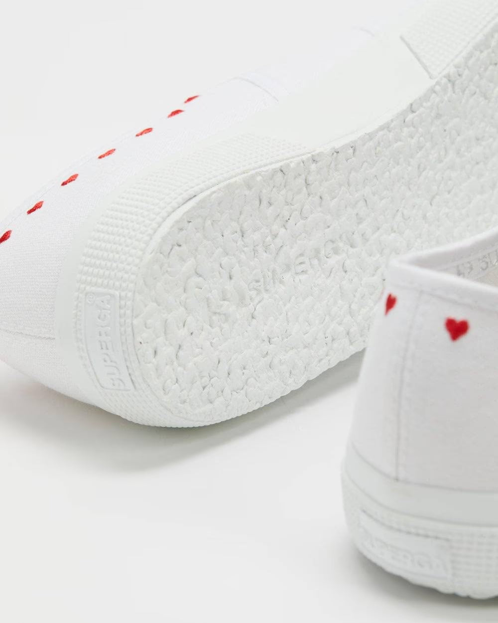 White low-top sneakers with red heart embroidery on side; textured rubber sole
