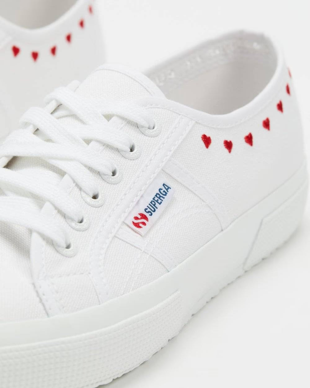 White lace-up low-top sneakers with red heart trim along side; SUPRA logo patch