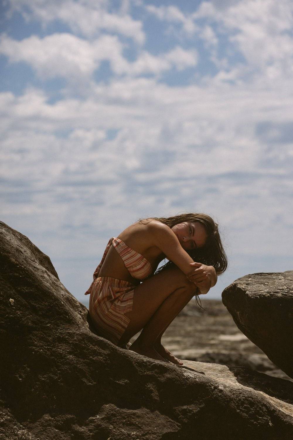 a woman sitting on top of a rock near the ocean